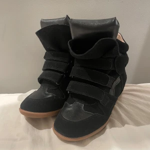 Svarta Isabel Marant sneakers - Coola svarta sneakers från Isabel Marant med högt skaft och chunky design. Skorna har flera kardborreband, detaljer i mocka och skinn samt en brun gummisula. Perfekta för dig som vill ha en edgy och trendig look. Priset kan diskuteras!!! Köpa här på Plick så har tyvärr inget äkthetsbecis!!!