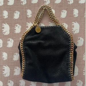Stella McCartney Falabella  - Hej! Har en Stella McCartney Falabella tiny tote som jag inte använder längre. Vill antingen byta mot annan märkesväska eller sälja. Har kvitto, dustbag och äkthetsbevis. Säljer helst för 4500 kr. Guldfärgen lite smått slitet vid handtagen men det syns knappt, väskan är i väldigt fint skick. Kram 🩷🩷