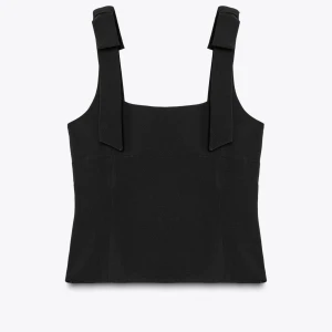 Svart linnetopp med breda axelband Zara - Stilren svart linnetopp från Zara med breda axelband och snygga knyt-detaljer upptill. Toppen har en rak, något croppad passform och är tillverkad i ett slätt, lätt stretchigt material som ger en modern look. Perfekt att matcha med jeans eller kjol.