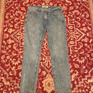 Blå jeans från Woodbird straight fit - Säljer ett par klassiska blå jeans från Woodbird med raka ben och normal passform. Jeansen har fem fickor, snygga kontrastsömmar och en läderpatch med logga bak i midjan. Perfekta för en clean och avslappnad look. Notera att lappen sitter löst:)