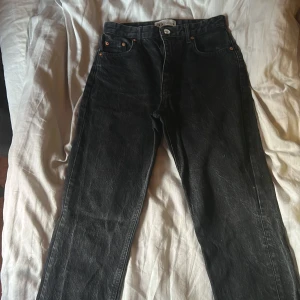 Svarta jeans med slits från Zara - Snygga svarta jeans från Zara i klassisk femficksmodell. Jeansen har hög midja, raka ben och coola slitsar nertill vid bensluten. Materialet är kraftig denim i bomull och färgen är tvättad svart för en lite vintage känsla.