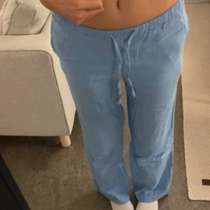 Ljusblå linnebyxor  - Säljer ett par ljusblå linnebyxor med avslappnad passform och elastisk midja med snörning. Byxorna har raka ben och praktiska sidofickor. 