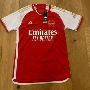 Arsenal tröja  - Rödvit Arsenal hemmaställ. Snygga guldiga detaljer på klubbmärket och ärmarna.