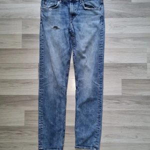 Slim fit ljusblå vintage jeans från H&M - Slim fit vintage jeans från H&M i ljusblå tvätt med slitna detaljer och klassisk femficksdesign. Jeansen har raka ben och normal passform, tillverkade i bomull. Perfekta för en avslappnad och trendig look.
