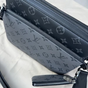 Väska - Snygg axelväska från  i grått och svart med klassiskt monogrammönster. Väskan har bred justerbar axelrem, flera fack med dragkedja och en matchande liten plånbok. Tillverkad i skinn med stilren design och silverfärgade detaljer. Kommer med orginal kort 