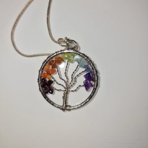 Halsband med regnbågsfärgat livets träd - Unikt halsband med ett runt hänge i silverfärgad metall, format som ett livets träd. Trädet är dekorerat med små stenar i regnbågens färger.