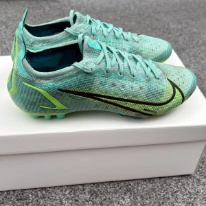 Fotbollskor Nike Mercurial Vapor 14 Elite AG - Snygga Nike Mercurial fotbollsskor i turkos med svarta och limegröna detaljer. Det är Elite verisionen, där av nypris cirka 2500. Bra skick överlag, lite slitna i hälen. Skorna passar 40-41. Pris kan diskuteras.