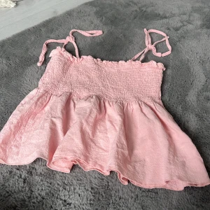 Rosa linnetopp från SHEIN med knytband - Supersöt ljusrosa linnetopp från SHEIN med smockad överdel och volangig nederdel. Toppen har tunna axelband som knyts på axlarna för en extra gullig touch. Perfekt för varma dagar och ger en luftig känsla.