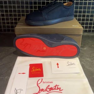 Mörkblå sneakers från Christian Louboutin - Exklusiva mörkblå sneakers från Christian Louboutin i mocka med ikonisk röd sula. Skorna har rund tå, snörning och diskreta detaljer på sidan. Insidan är ljusbeige och sulan är i gummi. Perfekta för dig som vill sticka ut med stil. Helt nya aldrig använda 10/10 skick