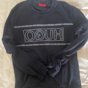 College-tröja Hugo Boss - College-tröja från Hugo Boss i svart med vit text i storlek M. 