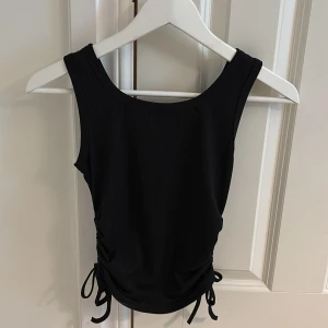 Svart ribbad linnetopp med snörning xs - Svart linne i storlek xs från shein. Snörning på sidan så man kan ändra längd på tröjan. Bra skick. 40kr