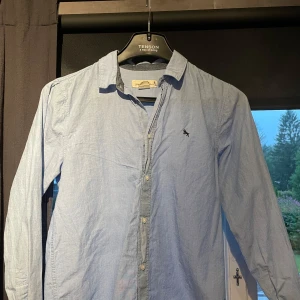 Ljusblå skjorta från Lexington storlek EUR 170 (ca XS) - Snygg ljusblå skjorta från Lexington med klassisk krage och broderad logga på bröstet. Skjortan har långa ärmar, knäppning framtill och är tillverkad i mjuk bomull. Perfekt för en clean och stilren look. Bra skicka om man strycker men men inga hål eller liknade