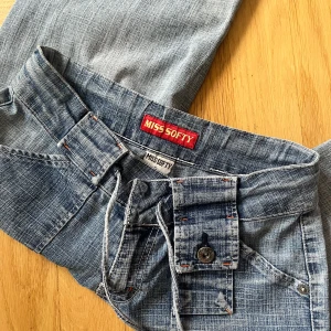 Blåa wide jeans från Miss Softy - Säljer ett par blåa jeans från Miss Softy. Byxorna har breda ben, snörning i midjan och stora fickor både fram och bak med knappdetaljer. Perfekta för en avslappnad och trendig look.
