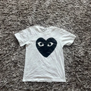 Vit Comme des Garçons Play t-shirt - Säljer en vit t-shirt från Comme des Garçons Play med det ikoniska svarta hjärtat med ögon tryckt på bröstet. Detta plagg är väldigt snyggt och säljs för jätte billigt pris.