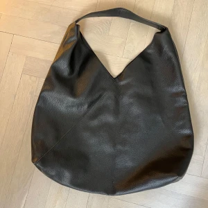 Svart axelväska i skinnimitation - Säljer en svart axelväska i skinnimitation med enkel och stilren design. Väskan har en mjuk struktur och rymlig insida, perfekt för att bära med sig det viktigaste till vardags. Passar dig som gillar minimalistisk stil.