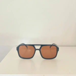 Snygga bruna solglasögon  - Snygga solglasögon med svart, kantig båge och bruna glas. Modellen har en modern, oversized känsla och passar perfekt för dig som vill sticka ut. Bågarna är i plast och har en cool retrovibe.