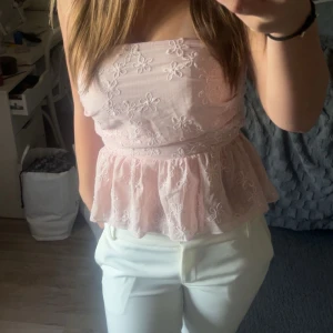 Ljusrosa broderad tubtopp med volang - Söt ljusrosa tubtopp med broderade blommor och volang nertill. Har gummi upptill så den inte åker ner. 