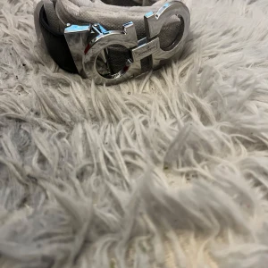 Svart bälte med silverfärgat spänne från Salvatore Ferragamo - Säljer ett svart bälte från Salvatore Ferragamo med ett stort, glänsande silverfärgat spänne. Bältet levereras med originalförpackning, dustbag och kvitto. Perfekt accessoar för att lyfta din outfit.