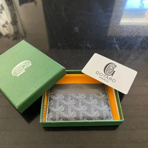 Grå korthållare  - Säljer ett stilrent grått kortfodral med ikoniskt mönster. Fodralet har flera kortfack och är tillverkat i skinn med detaljer i grått och vitt. Perfekt accessoar för att hålla ordning på dina kort.