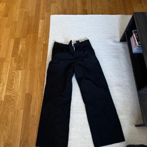Svarta kostymbyxor från Weekday - Säljer ett par svarta kostymbyxor från Weekday. Byxorna har klassisk rak passform med hällor för bälte och stängs med knapp och dragkedja. Perfekta för en stilren look.