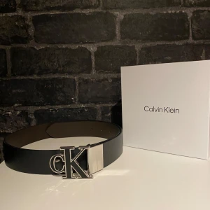 Svart bälte från Calvin Klein - Snyggt svart bälte från Calvin Klein med ett stort metallspänne i silver med CK-logga. Bältet är stilrent och passar perfekt till jeans eller kostymbyxor. Levereras i originalförpackning.