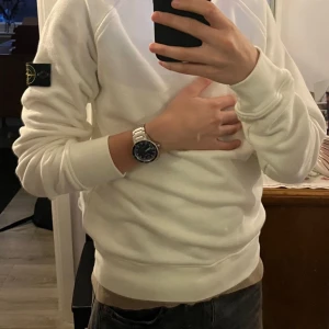 Vit sweatshirt från Stone Island - Säljer en stilren vit sweatshirt från Stone Island med klassisk logotyp-patch på vänster ärm. Tröjan har rund halsringning och ribbade muddar vid ärmslut och nederkant. Perfekt för en clean och avslappnad look. Kvitto och prislapp kommer med. Priset kan diskuteras vid snabb affär!!