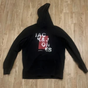 Svart hoodie från Jack & Jones - Svart hoodie från Jack & Jones med tryck framtill. Har två små hål på höger och vänster arm men syns knappt.
