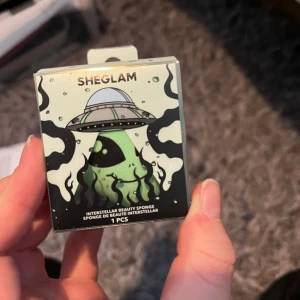 SHEGLAM Interstellar Beauty Sponge - En beautyblender från SHEGLAM i en cool förpackning med rymdtema och ufo-illustration. Perfekt för att applicera foundation eller concealer jämnt och smidigt. Kommer i originalförpackning. ALIEN