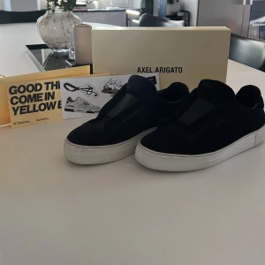 Svarta sneakers från Axel Arigato - Säljer ett par svarta clean 360 Laceless skor från Axel Arigato i storleken 43. Skon har en vit platt sula och diskret logga på sidan. Säljer dessa skor eftersom jag är sugen på ett par nya. Ny pris är 2550 kr och mitt pris är 1275 kr (köparen står för frakten). Tycker det är ett fair pris eftersom jag har box och de är i ett mycket bra skick. Perfekta för dig som gillar stilrena och trendiga skor. Skriv bara om du har frågor!
