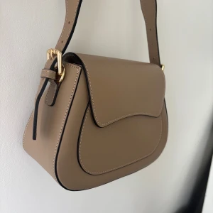 Latalia handväska (oanvänd!) - En jättefin brun/beige Latalia väska med både långt och kort handtag (båda går att ta av och på). Skriv för fler bilder, ex på insidan av väskan. Nypris var 1395kr och den är helt oanvänd. 