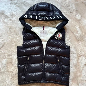 Moncler Väst  - Unik moncler väst med luva. Självklart äkta. Storleken är 14 year old. Men passar XS utan tvekan. Modellen är 180cm/60kg. Skriv angående fler bilder på industitagen, qr koden eller cartoonen. 