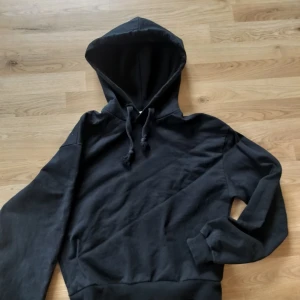 Svart hoodie från NA-KD - Säljer en svart hoodie från NA-KD i storlek M. Tröjan har huva med dragsko och långa ärmar med muddar. Perfekt för en avslappnad och stilren look.