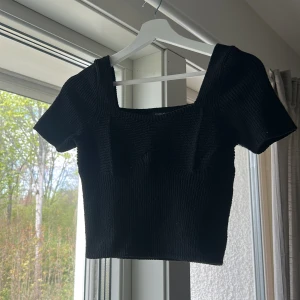 Svart croppad topp med fyrkantig ringning - Säljer en svart croppad topp med korta ärmar och fyrkantig ringning. Toppen är ribbad och har en tight passform, perfekt att styla till olika outfits.