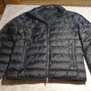 Mörkblå jacka Gant  - Säljer en helt oanvänd  svart pufferjacka från Gant i storlek M. Jackan har dragkedja framtill och två sidofickor med dragkedja. Lätt och smidig modell med ståkrage, perfekt för våren