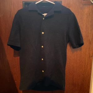 Svart kortärmad sommar skjorta från Zara - Säljer en svart kortärmad skjorta från Zara med klassisk krage och knappar framtill. Skjortan har en lätt textur i tyget och passar perfekt till sommaren. Enkel och stilren design som funkar till många tillfällen. Storlek s, säljer för 150