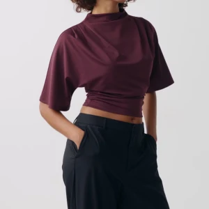 Vinröd topp/blus ifrån Gina tricot - Snygg vinröd croppad topp i satin med hög hals och korta vida ärmar. Perfekt för att lyfta din outfit med en elegant touch.