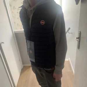 Mörkblå dunväst från Colmar - Snygg mörkblå dunväst från Colmar med hög krage och två dragkedjefickor framtill. Västen har Colmar-logga på bröstet och stängs med dragkedja. Perfekt för lager-på-lager och stilrena outfits.