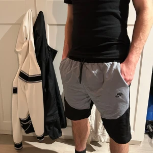 Svarta shorts från Nike - Svarta shorts från Nike med enkel design och diskret logga på vänster ben. Shortsen har elastisk midja med snörning för justerbar passform. Perfekta för träning eller avslappnade dagar.