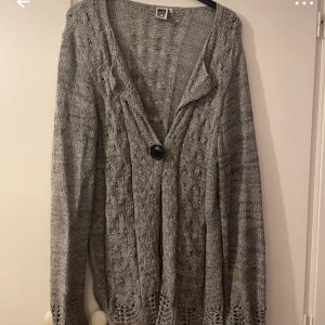 Grå stickad kofta från Isolde - Säljer en lång, grå stickad kofta från Isolde i storlek XL. Koftan har ett snyggt kabelstickat mönster, en stor knapp framtill och långa ärmar. 