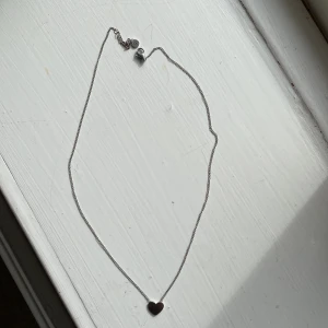 Halsband med hjärta i silverfärg - Säljer ett stilrent halsband i silverfärg med ett litet hjärta som hänge. Kedjan är tunn och smidig, perfekt för att bära varje dag. Hjärtat ger en söt och enkel touch till din outfit. Halsbandet är från edblad och är i rostfrittstål.