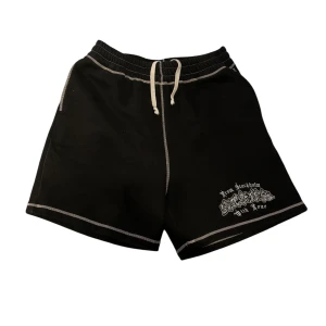 Svarta shorts med vit brodyr och kontrastsömmar från Seams  - Svarta shorts från Seams med vita kontrastsömmar och snörning i midjan. Broderad text och motiv framtill samt en broderad hund på bakfickan. Perfekta för en avslappnad stil. Storlek L.