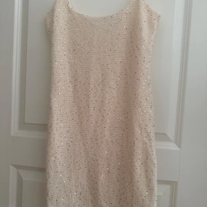 Glittrig ljusbeige paljettklänning - Säljer en glittrig ljusbeige klänning med paljetter och smala axelband. Klänningen har rak passform och är ärmlös.