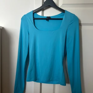 Turkos långärmad topp från Vero Moda - Säljer en turkos långärmad topp från Vero Moda med fyrkantig ringning. Sitter tight och är gjord i ett mjukt, stretchigt material. Perfekt att styla med jeans eller kjol för en fräsch look.