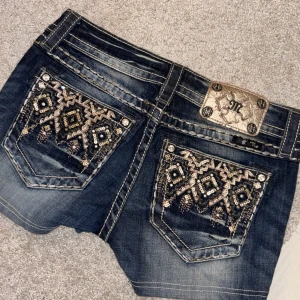 Jeansshorts med paljettdetaljer från Miss Me - Mörkblå lågmidjade jeansshorts från Miss Me med snygga slitningar och dekorativa bakfickor med paljetter i mönster. Aldrig använt säljer då den inte passar mig❤️ ny pris runt 1500-2000 (tror jag) säljer för 600! Storklek w26/S