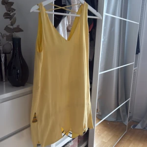 Gul ärmlös klänning från Animale - Säljer en solgul ärmlös klänning från Animale med v-ringning och ojämn nederkant. Klänningen har en luftig passform och är perfekt för varma dagar. Materialet känns lätt och svalt mot huden. ny pris 2000kr