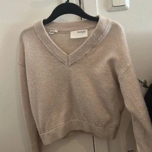 Beige v-ringad stickad tröja från Selected Femme - Mysig beige stickad tröja från Selected Femme med v-ringad hals och ribbade muddar. Perfekt för lager-på-lager och passar till både jeans och kjol. Enkel och stilren design. Använd några gånger 