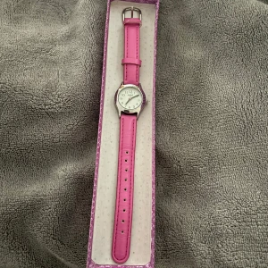 Rosa klocka från uropenn  - Säljer en stilren klocka från Regal med rosa skinnarmband och silverfärgat runt ur. Klassisk vit urtavla med tydliga siffror. Perfekt accessoar för att sätta färg på outfiten!