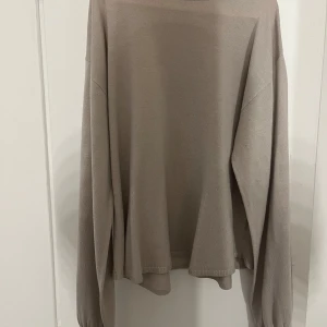 Beige stickad tröja med lång ärm - Säljer en beige stickad tröja med lång ärm och avslappnad passform. Tröjan har rund halsringning och är lite lös nertill, vilket ger en skön och ledig känsla. Perfekt för lager-på-lager under kyligare dagar.
