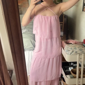 Ljusrosa långklänning med volanger - Säljer en romantisk ljusrosa långklänning med tunna axelband som korsas i ryggen. Klänningen har flera lager volanger och är ärmlös, vilket ger en luftig och somrig känsla. Perfekt för varma dagar eller speciella tillfällen.💗Bara hör av er för fler bilder samt frågor 