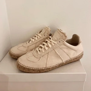 Beige sneakers från Maison Margiela - Snygga vita skor från Maison Margiela med en mycket unik design. Skorna är tillverkade i canvasöverdel och passar perfekt nu till sommaren! Skorna är helt nya, skopåse och box medföljer.